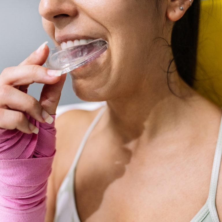 Midsection of a female athlete putting on a mouth guard in boxing training in a ring.