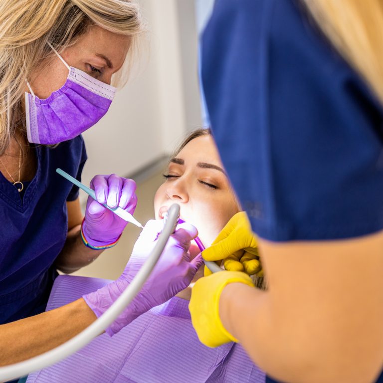 Female dentist with assistant working in dental clinic examining patient teeth.