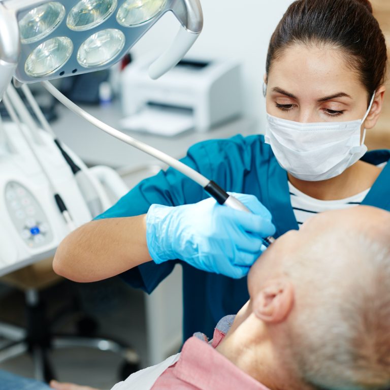 Dentist drilling sick tooth of senior patient before putting filling