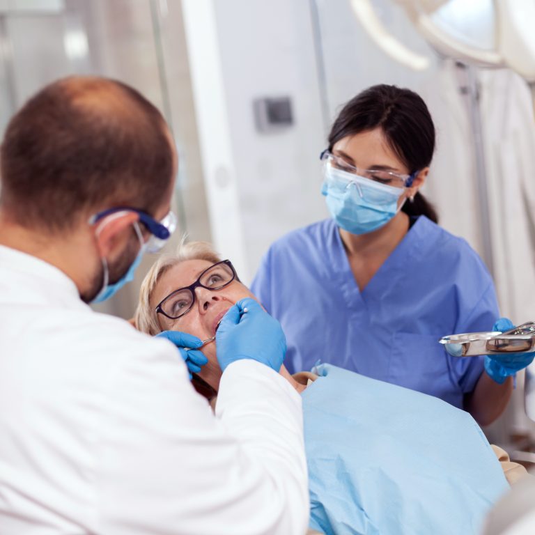 Dentist with assistant install implant in patient mouthin modern clinic. Elderly woman during medical examination with stomatolog in dental office with orange equipment.