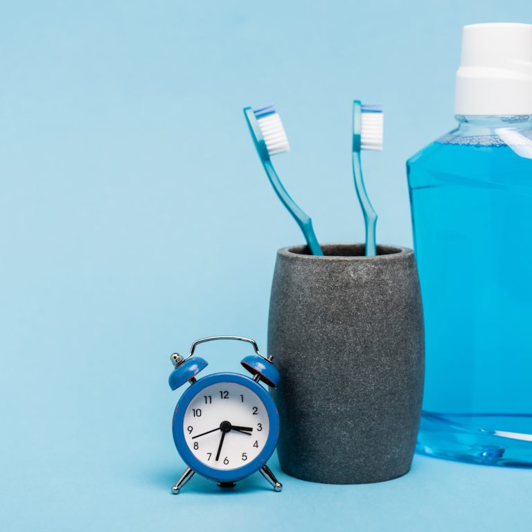 Toothbrushes near mouthwash and small alarm clock on blue background